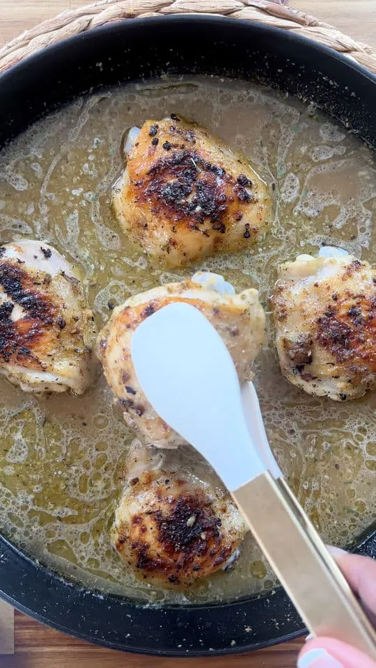 Cooking seasoned chicken thighs in a skillet with a spatula.