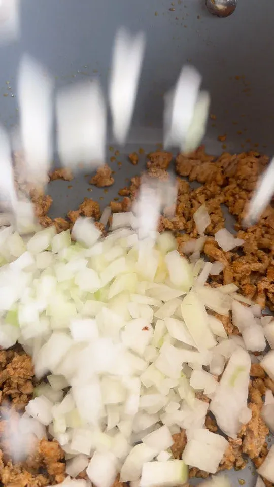 Chopped onions falling into a pan with browned ground meat.