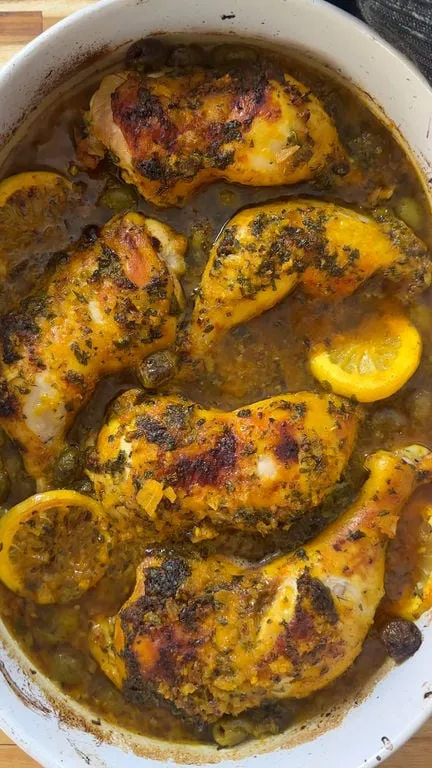 Roasted chicken with herbs and lemon slices in a white dish.