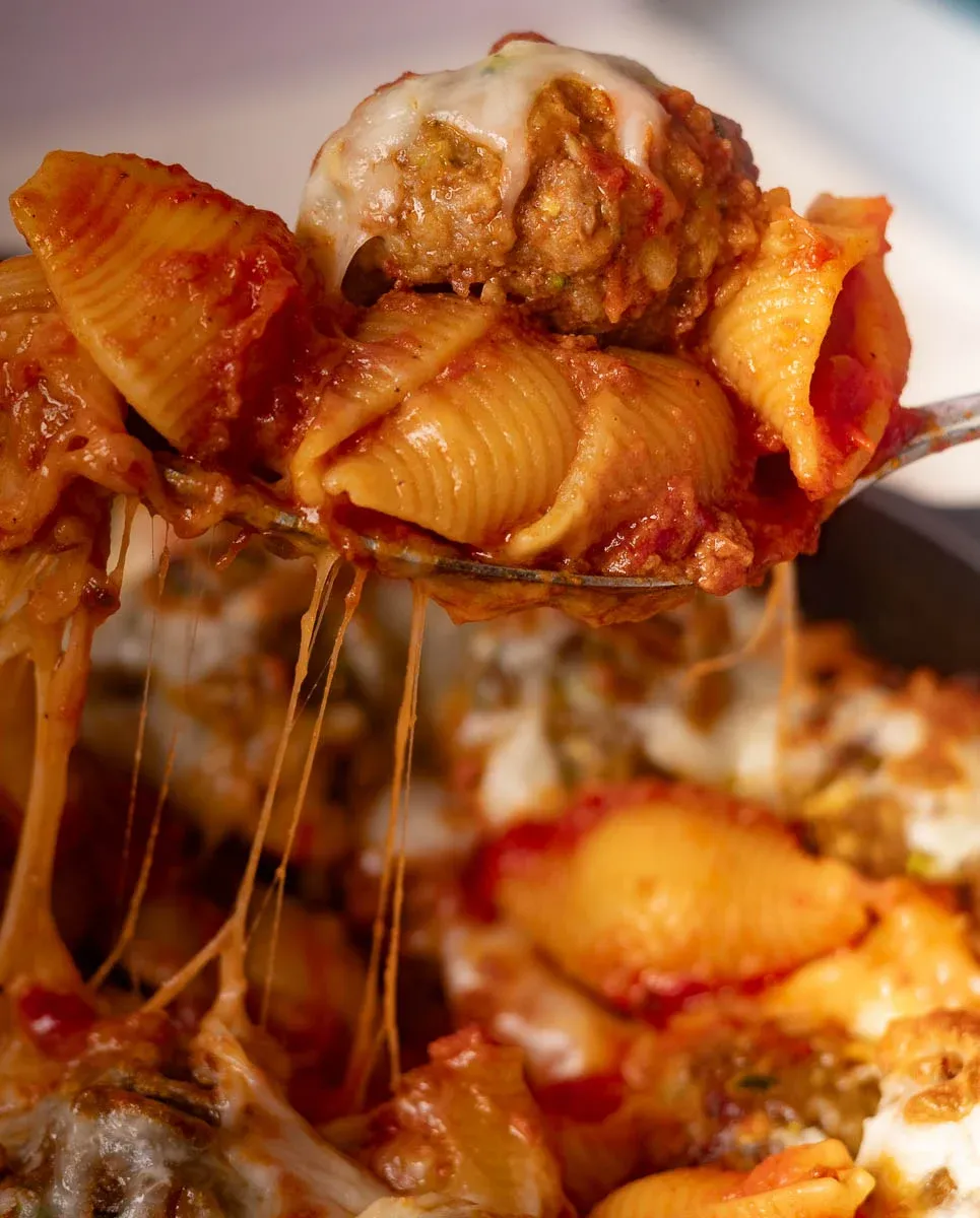 Cheesy baked meatballs and pasta in tomato sauce on a fork.