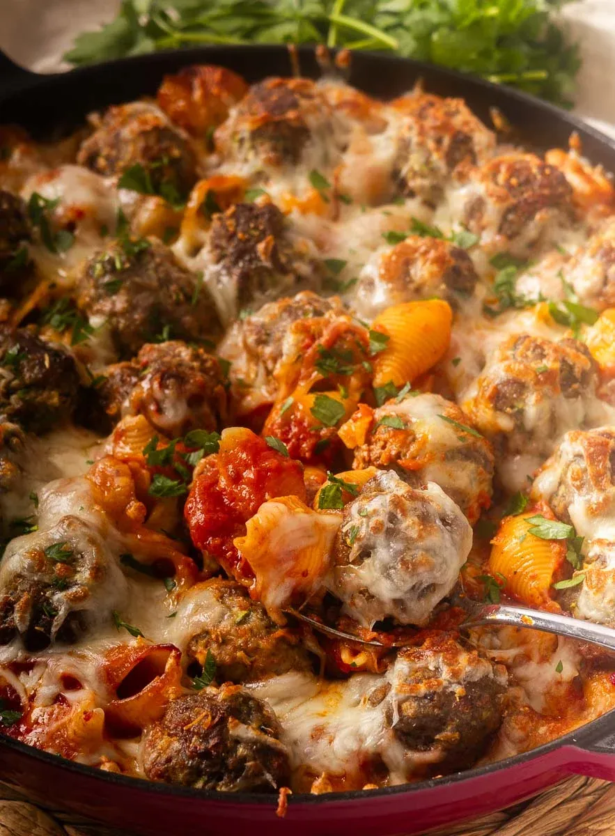 Cheesy baked meatballs and pasta with tomato sauce and herbs in a skillet.