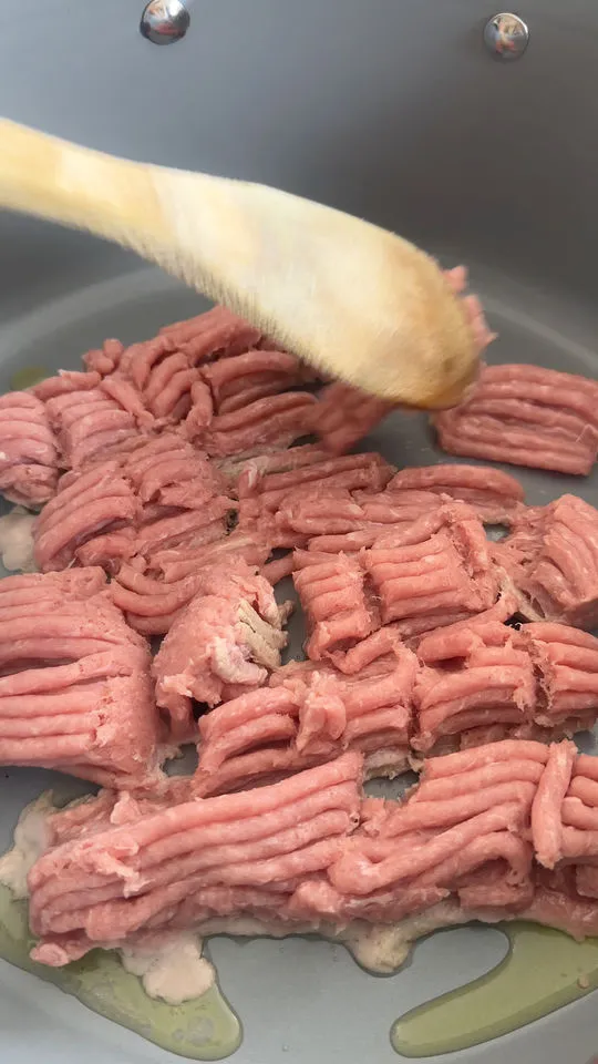 Raw ground meat being stirred in a pan with a wooden spoon.