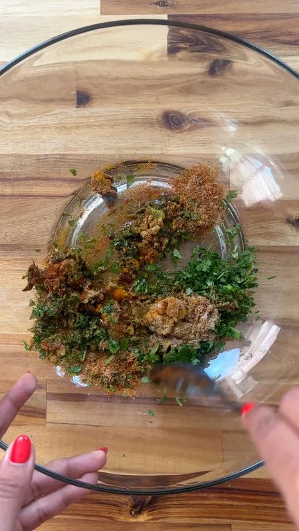 Mixing fresh herbs and spices in a clear bowl on a wooden surface.