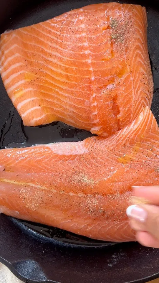 Two fresh salmon fillets seasoned with pepper in a black pan.