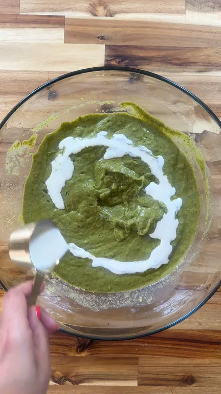 Pouring cream into a bowl of green soup.