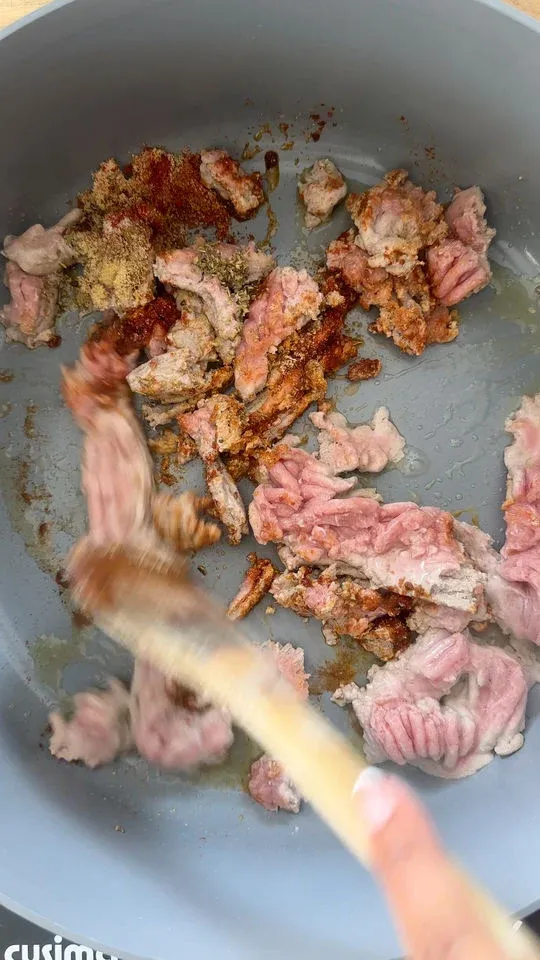 Cooking ground meat with spices in a gray pan, wooden spoon stirring.