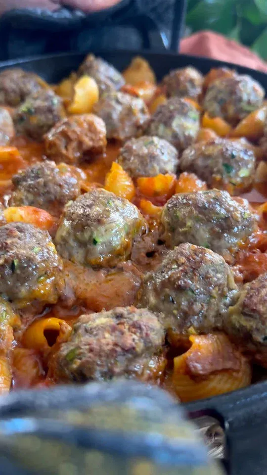 Meatballs and pasta shells baking in tomato sauce inside a black pan.