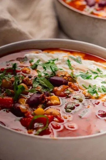 Bowl of Mediterranean bean stew with kidney beans, vegetables, and parsley garnish, topped with a dollop of sour cream.