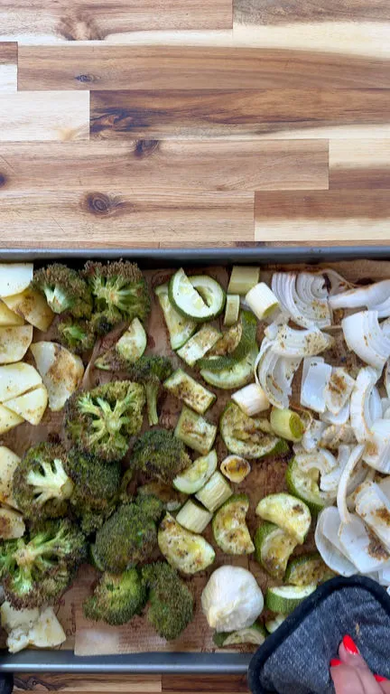 Roasted vegetables on a tray including broccoli, onions, and zucchini, seasoned with spices.