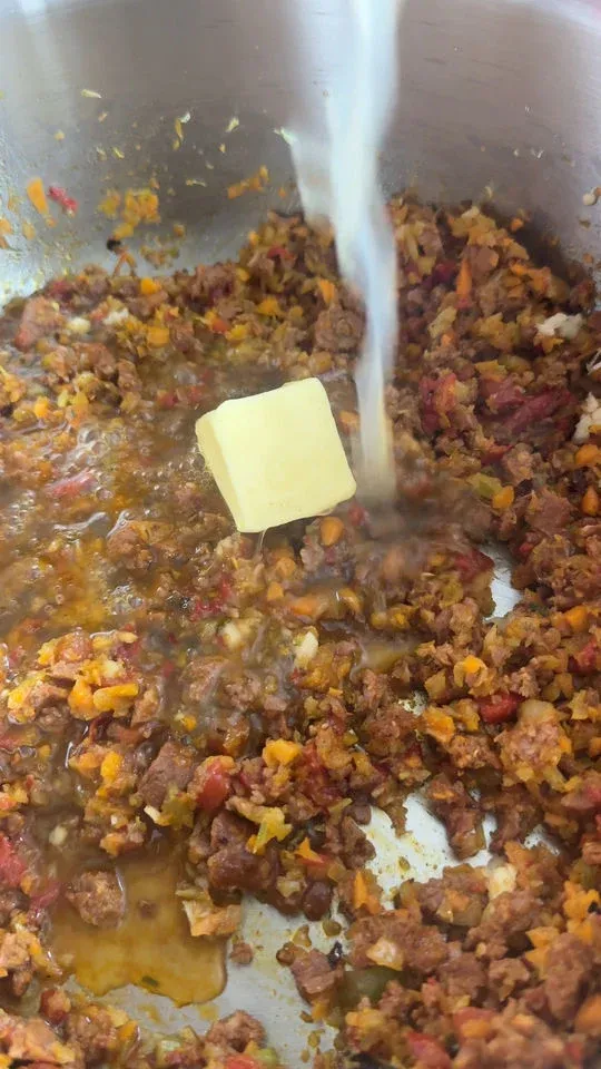 Cooking chorizo with carrots, spices, and a melting butter cube in a pan with added liquid.