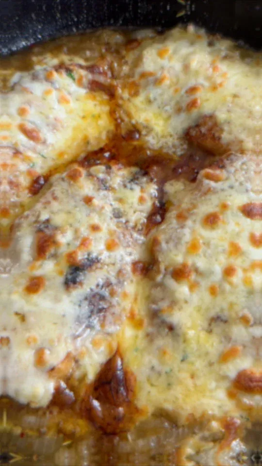 Cheesy chicken breast with melted cheese topping, baked to golden perfection in a black skillet.