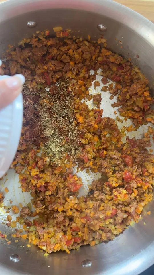 Cooking minced vegetables and ground meat with spices in a stainless steel pan.