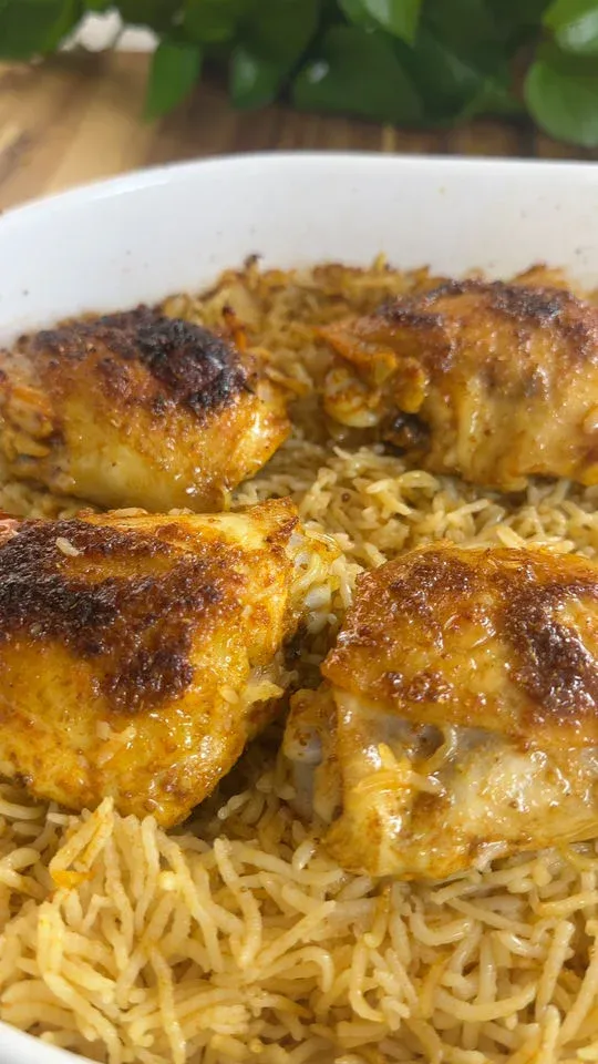 Baked chicken with crispy skin on a bed of seasoned rice in a white dish.