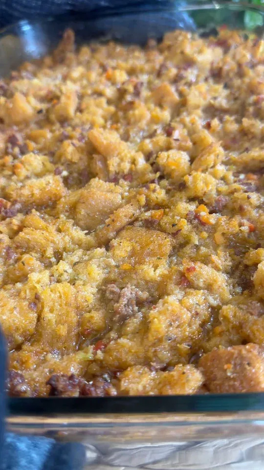 Close-up of baked cornbread stuffing with visible chunks of bread and crispy edges in a glass baking dish.