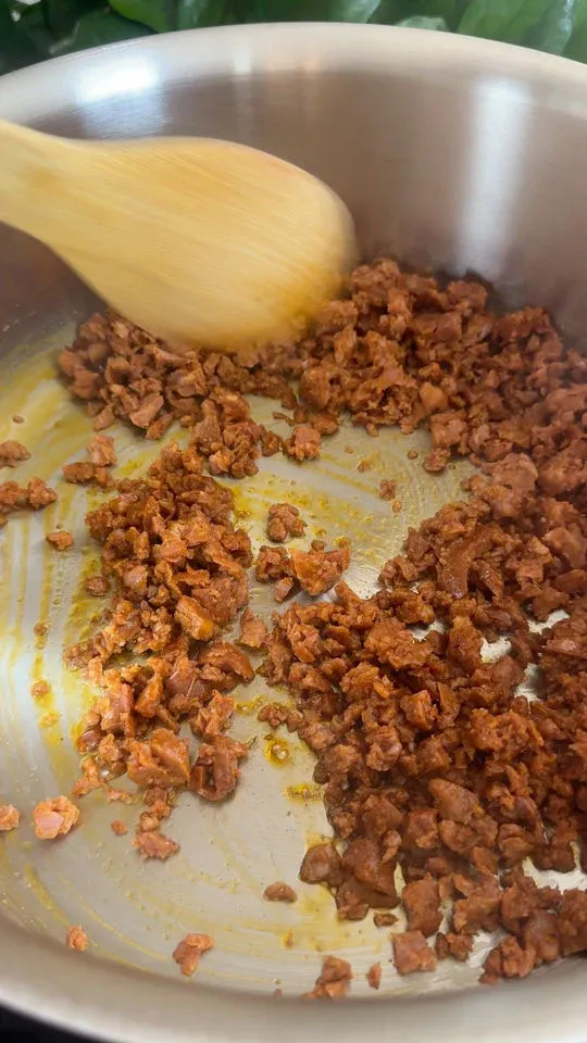 Cooking chorizo in a stainless steel pan with a wooden spoon stirring.