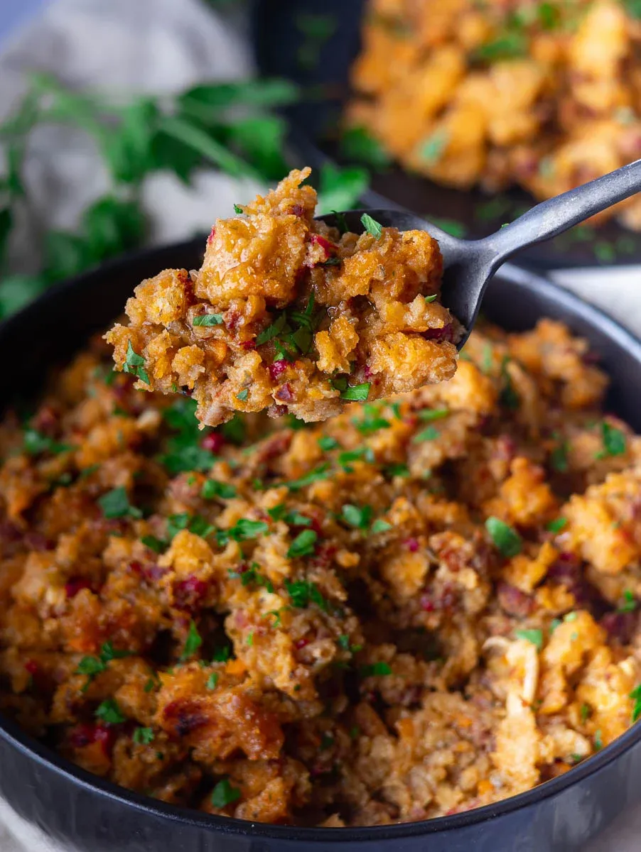 Close-up of a spoonful of Chicken chorizo and stuffing casserole garnished with chopped parsley in a black bowl.