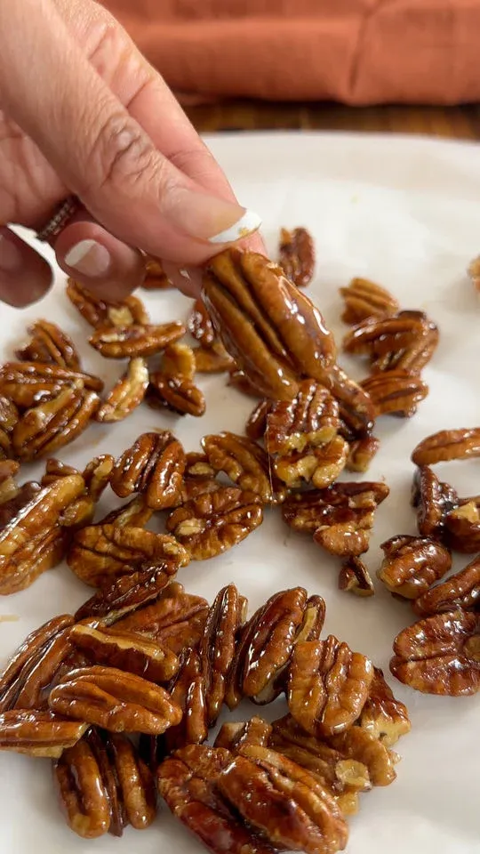 Hand holding glazed pecan over a tray of glazed pecans.
