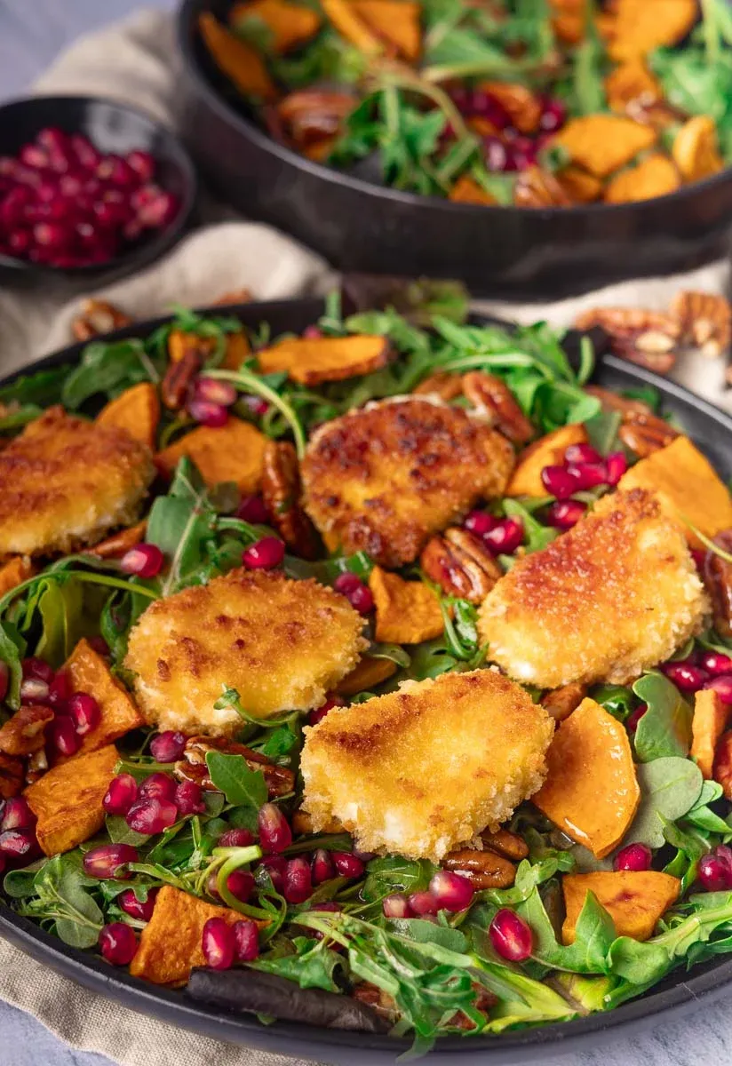 Crispy goat cheese salad with goat cheese salad with arugula, sweet potatoes, pomegranate seeds, and pecans.