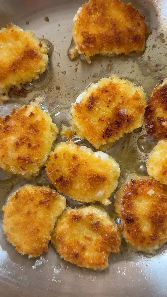 Golden-brown breaded goat cheese frying in a pan with oil.