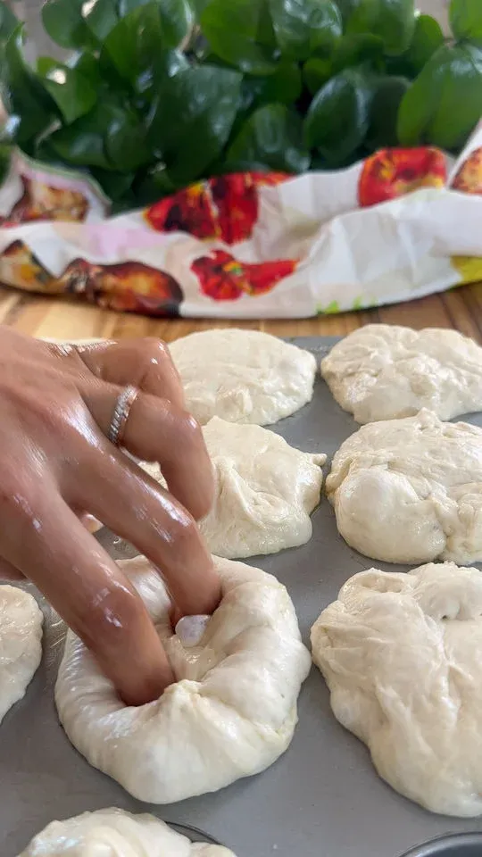 Hand shaping dough balls on a tray with leaves and a colorful cloth in the background.