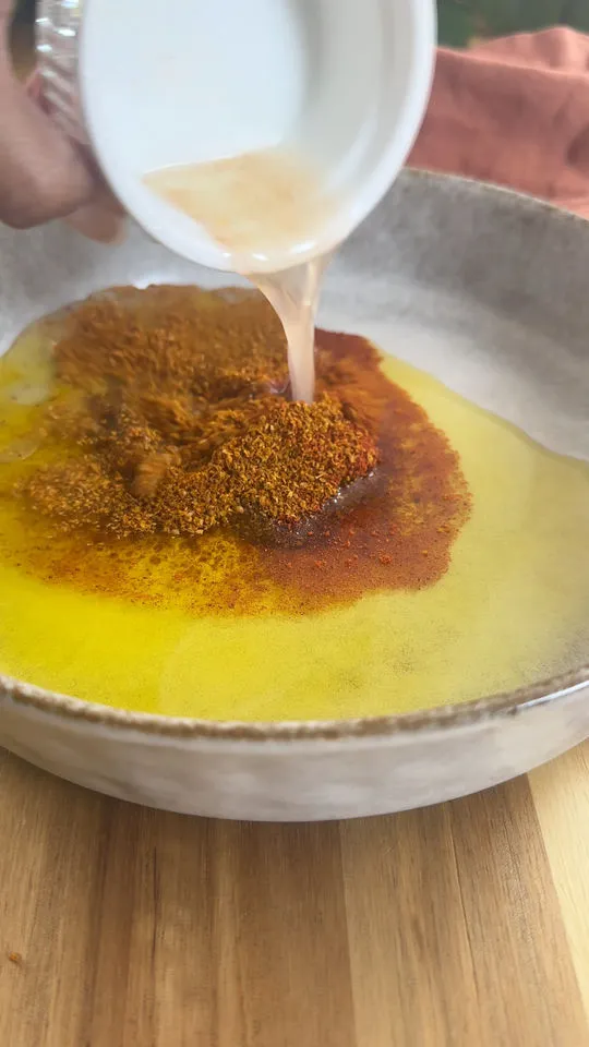 Pouring lemon juice into bowl with oil and spices on wooden surface.