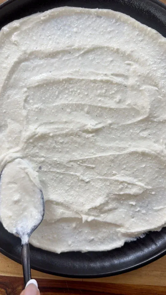 Spreading whipped feta with a spoon on a black round pan.