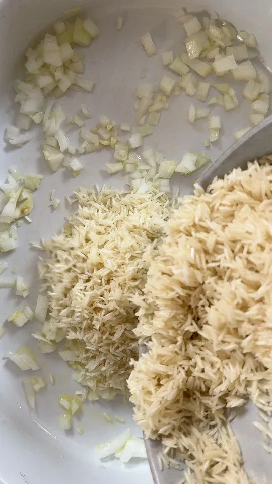 Chopped onions and uncooked rice in a white pot, prepped for cooking.