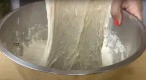 Hands stretching sticky dough in a metal mixing bowl.