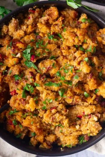 Bowl of savory Chicken chorizo and stuffing casserole with herbs and cranberries.