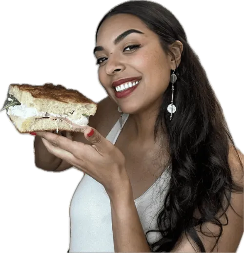 Smiling woman holding a large sandwich with layers of meat and lettuce.