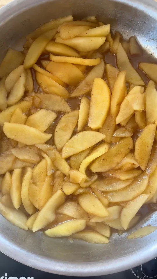 Sliced apples cooking in a pan with cinnamon and sauce.