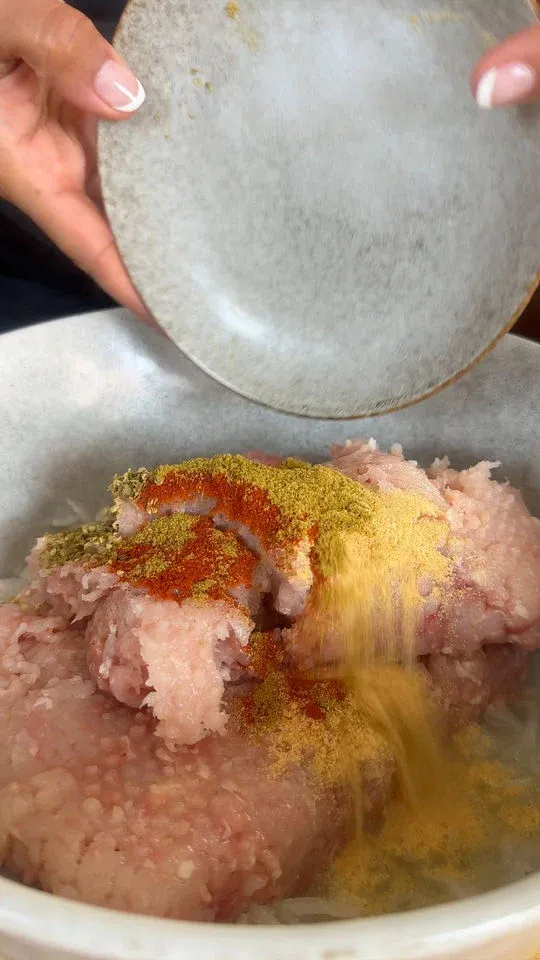 Adding spices to ground meat in a bowl for cooking.