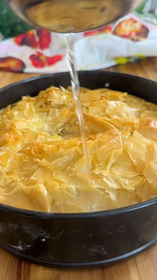 Pouring syrup over freshly baked baklava in a round pan.