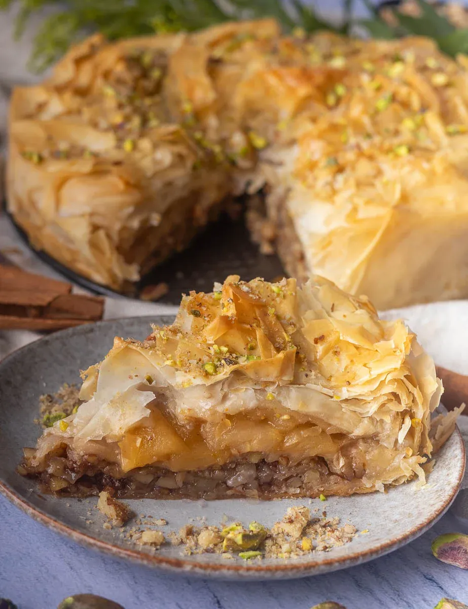 Slice of apple pie baklava on a plate with layers of phyllo pastry, nuts, and honey, garnished with crushed pistachios.