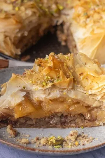 Slice of apple pie baklava on a plate, topped with crushed pistachios and flaky pastry layers.
