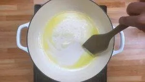 Cooking butter melts in a white pot with a spatula, on a wooden counter.