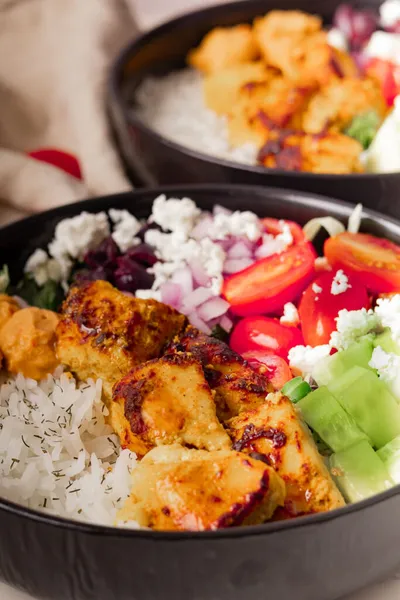 Chicken Mediterranean Bowl with tomatoes, cucumber, feta cheese, onion, and hummus in a black bowl.