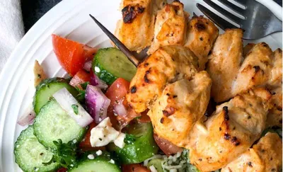 Grilled chicken skewers with a fresh cucumber tomato salad on a white plate.
