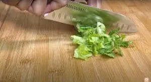 Chopping fresh green lettuce on a bamboo cutting board with a chef's knife.