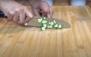Person chopping cucumber on a bamboo cutting board with a chef's knife, close-up view.