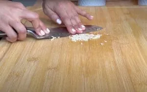 Close-up of hands finely chopping garlic on a wooden cutting board with a chef's knife.