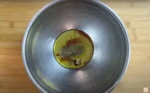 Olive oil, spices, and seasoning mix in a metallic bowl on a wooden surface for a homemade dressing recipe.