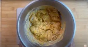 Marinated chicken pieces in a metal bowl, ready for cooking with spices on a wooden surface.