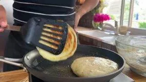Person flipping fluffy, golden pancakes in a skillet in a bright kitchen.
