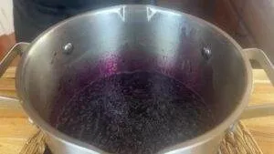 Pot of bubbling dark purple jam mixture on a stove, highlighting cooking process and rich color.