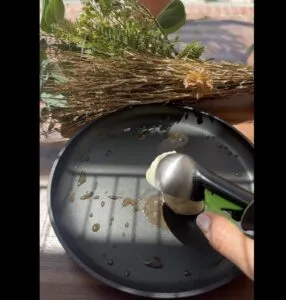 Scooping pancake batter onto a hot frying pan with sunlight and foliage in the background.