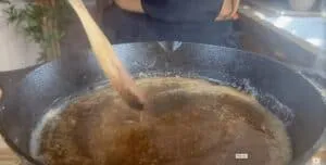 Person stirring sauce in a cast iron skillet with a wooden spoon in a kitchen setting.