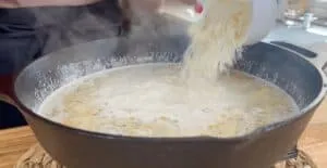 Adding grated cheese to creamy sauce in a cast iron pan, creating a delicious, savory dish.