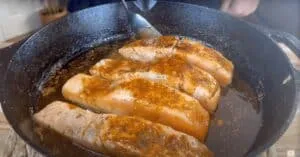 Pan-seared salmon fillets with seasoning in a cast iron skillet.