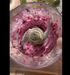 Food processor blending vibrant pink mixture in sunlight. Culinary preparation process with creamy texture.